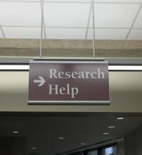 The photo displays a sign hanging down from the ceiling with an right arrow and text Research Help on it.
